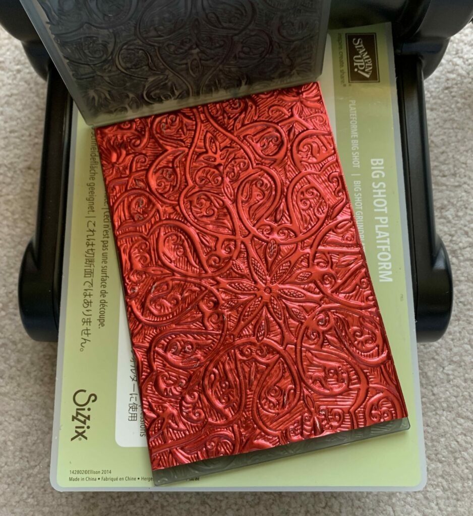 Metallic red cardstock embossed with the engraved embossing folder by Sizzix.